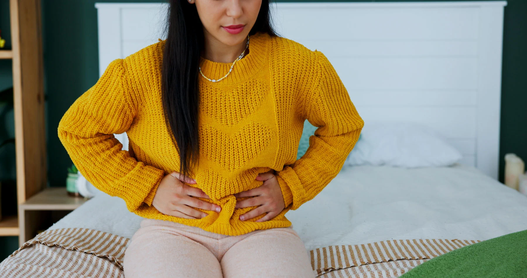 Woman holding her lower abdomen while seated on a bed