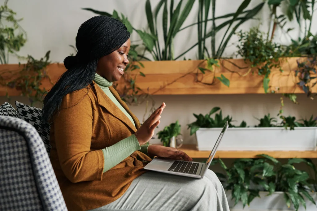 Woman smiling while working on a laptop in a plant-filled room